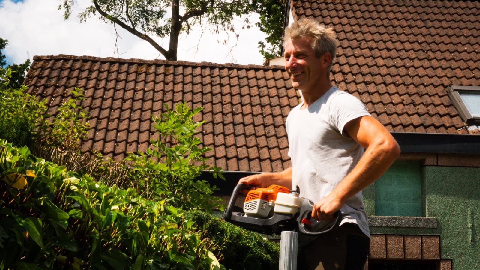 The landscaper smiling, hedge trimmer in hand, in front of a house